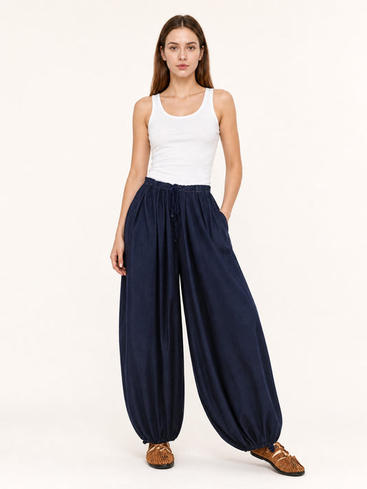 Dark blue pants shown full-body on a model, with an elastic drawstring waist, side pockets, wide legs, and gathered ankle hems