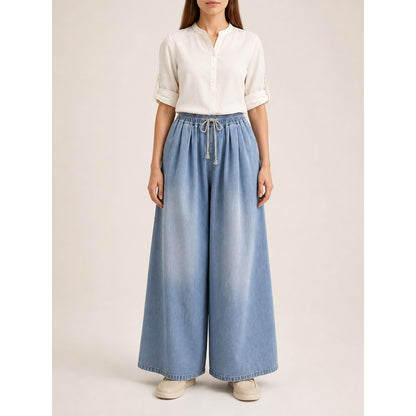 The model features a relaxed style with very wide, full-length legs that create a laid-back silhouette and suit everyday looks. The light blue shade with a subtle denim-like effect makes the piece versatile for warm weather and easy to pair