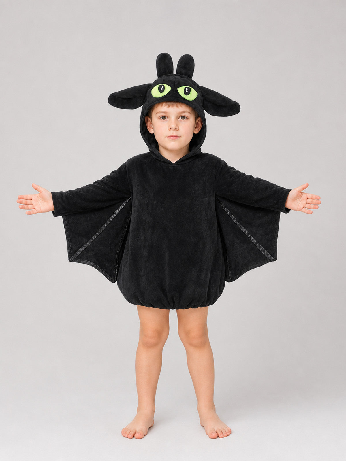 Black plush bat costume shown full-body on a child, with hood, upright ears, large eyes, and outstretched wing panels