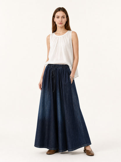 Full-body model wearing dark blue denim-look palazzo pants with a drawstring waist, styled with a sleeveless white top