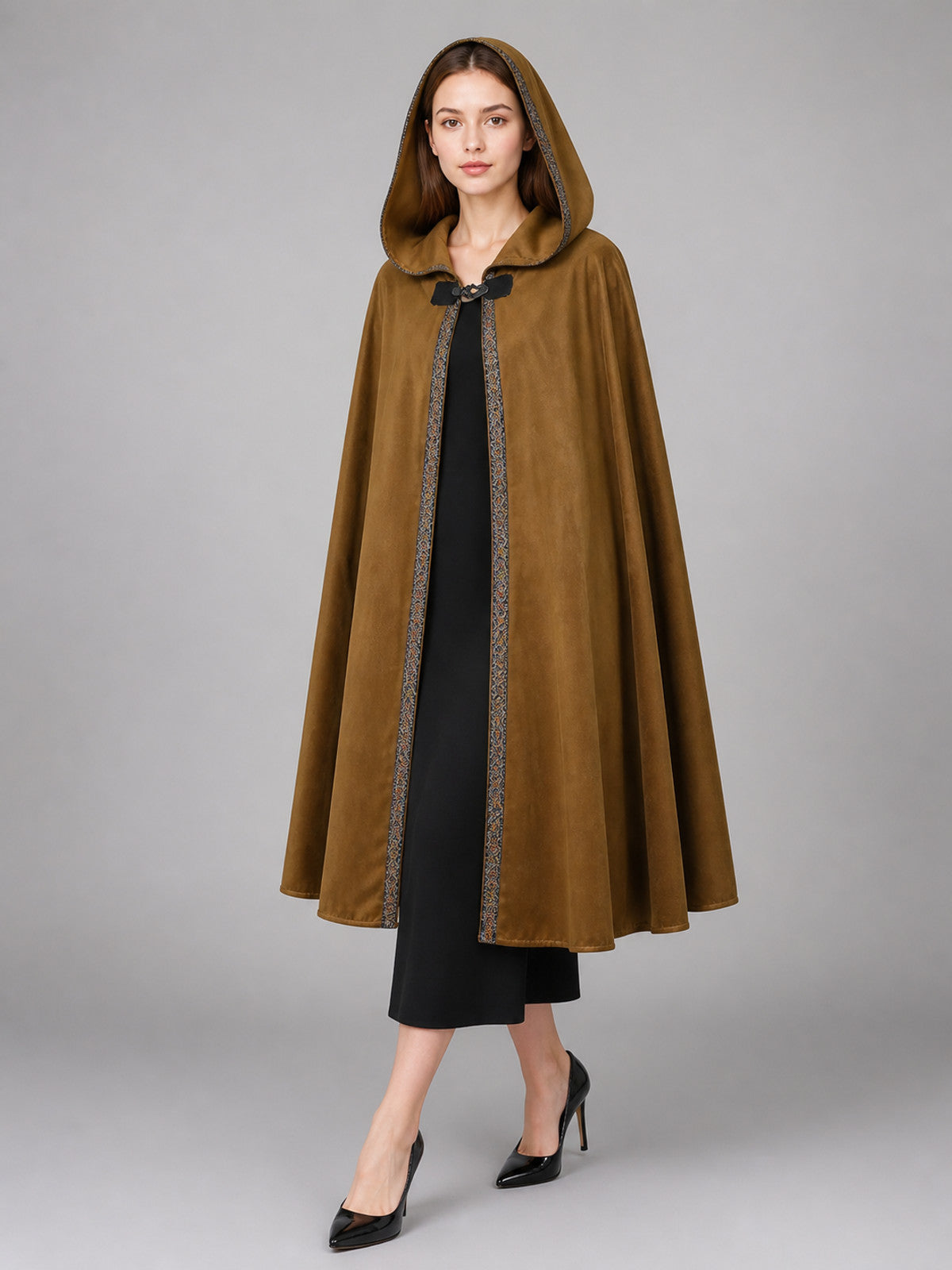 Brown suede-like hooded cape modeled full-body over a black dress, with patterned trim, front tie, and flared hem