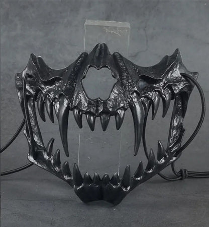 Actual product photo of the black skull jaw half mask with fangs and black cord ties, shown on a clear display stand (stand not included)