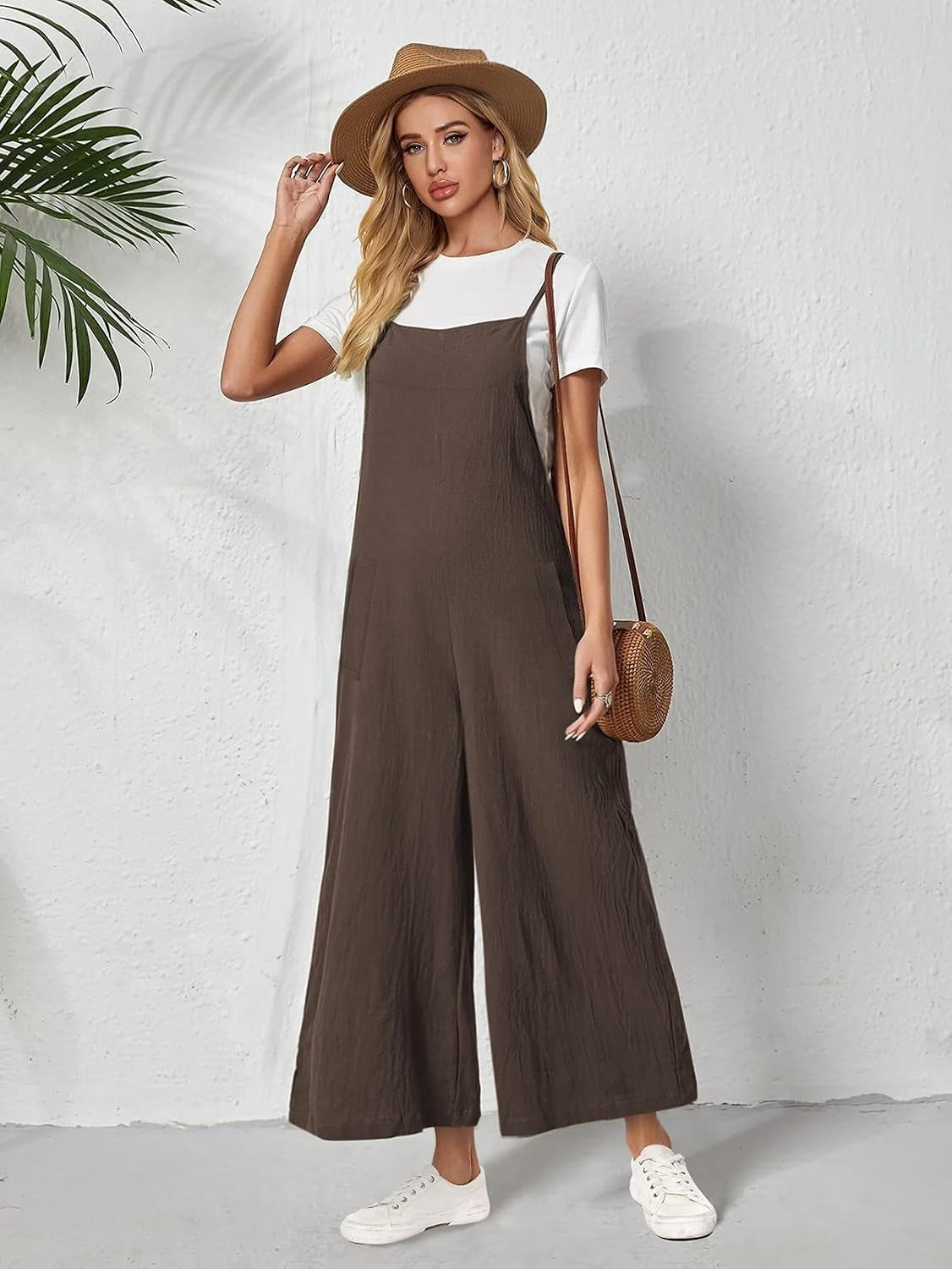 Model in brown cotton linen wide-leg overalls worn over a white T-shirt, showing the side pocket and crinkled linen texture