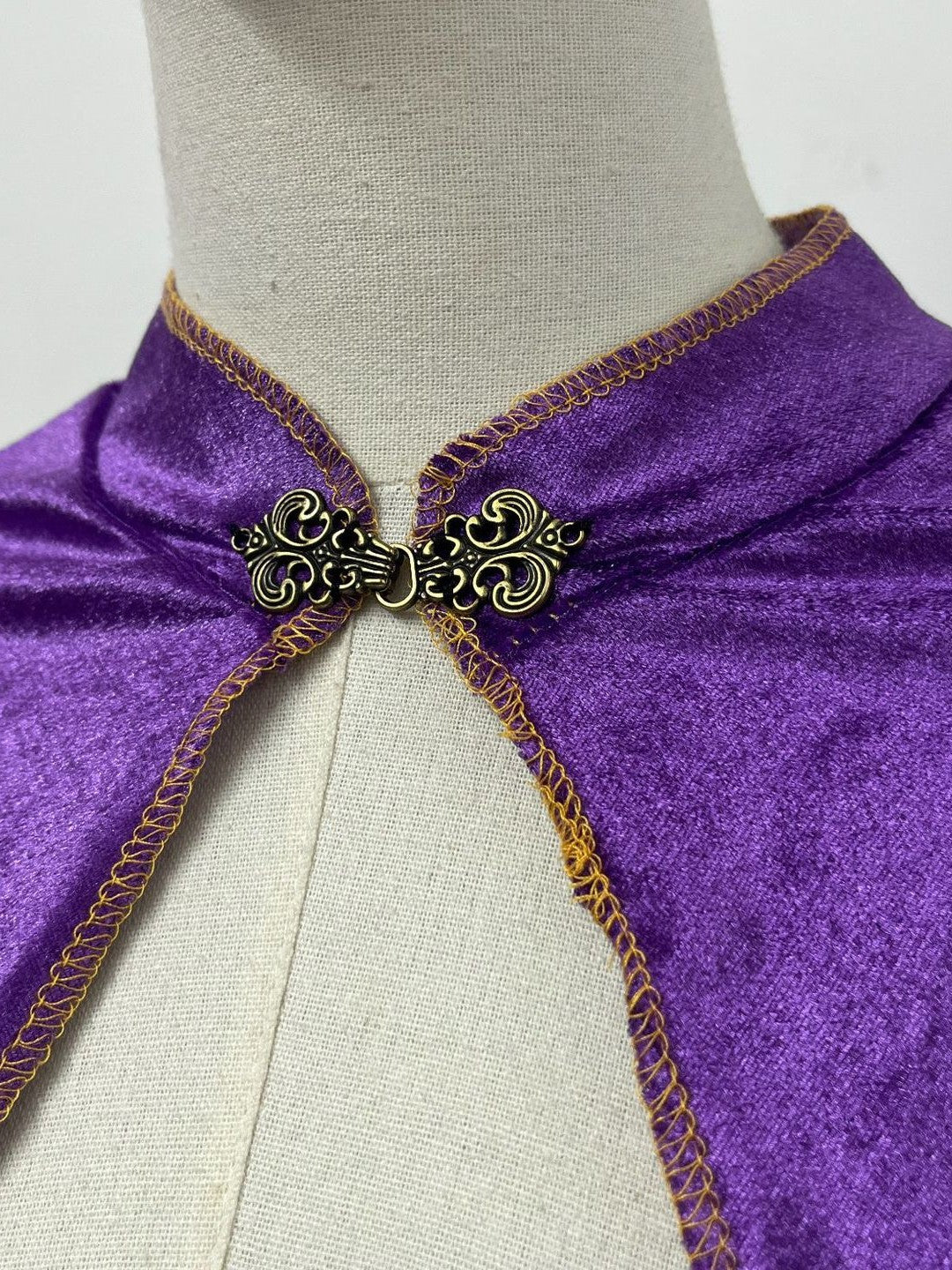 Close-up of the ornate metal-look clasp, stand-up collar and gold-tone stitched trim on the purple velvet cloak