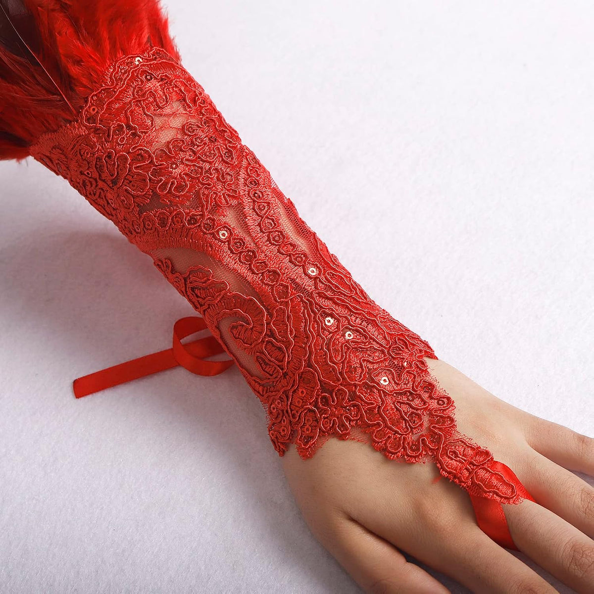 Close-up of the red sequin lace glove showing the satin ribbon finger loop and wrist tie