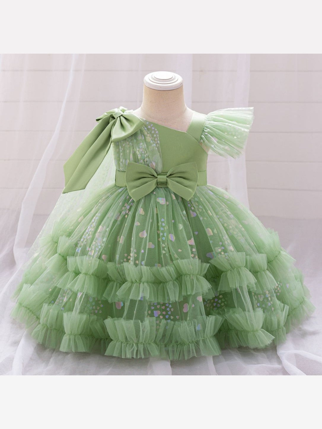 Avocado green toddler princess dress on a child mannequin, front view: shoulder bow, flutter sleeve, waist bow and tiered heart-print tulle ruffles