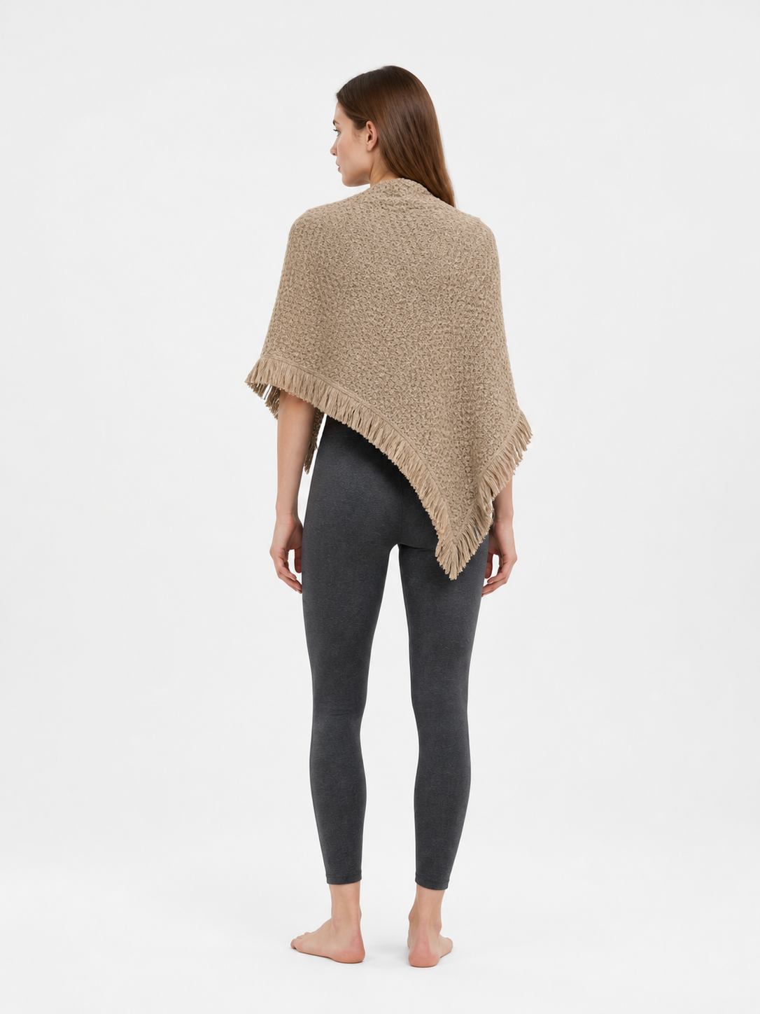 Back view of the beige textured cape over wide-leg light trousers, showing its triangular shape and fringe along the hem