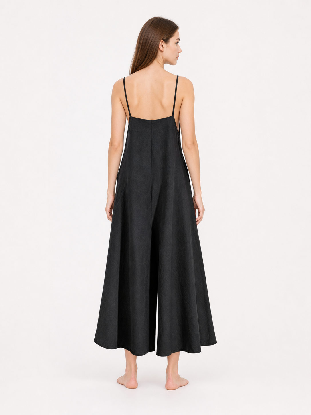 Back view of a black wide-leg jumpsuit showing thin shoulder straps and the loose flowing shape on a barefoot model