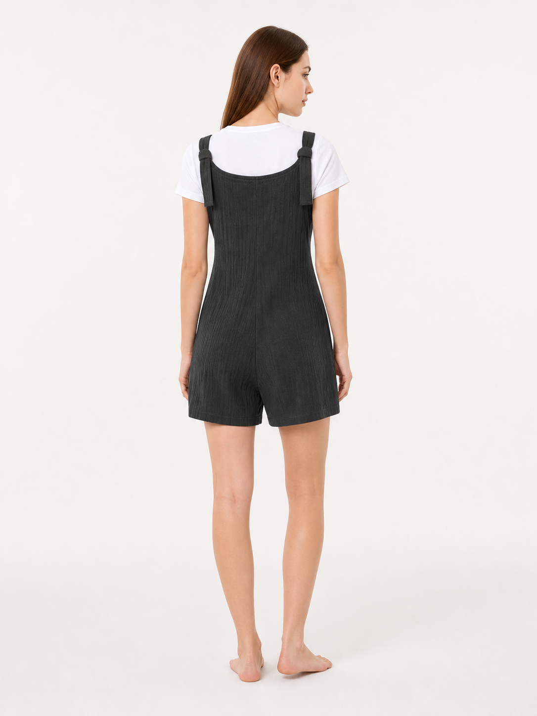 Back view of black textured bib shorts with shoulder straps, shown on a model wearing a white T-shirt