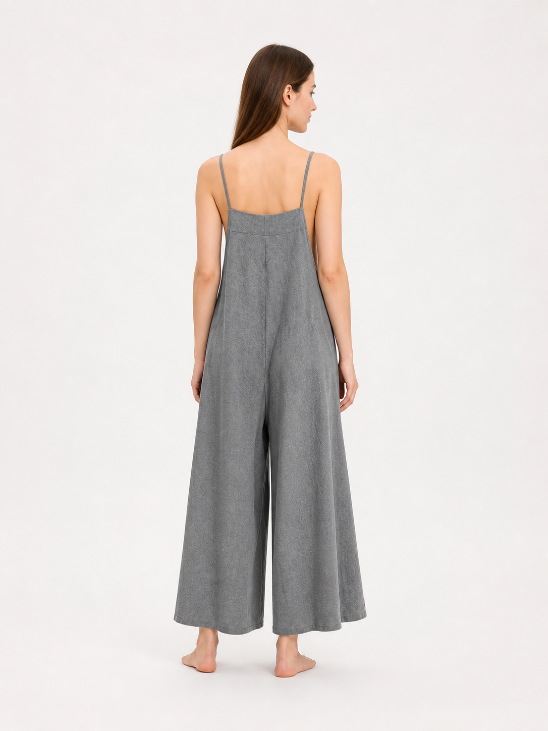 Back view of a gray wide-leg jumpsuit on a model, showing thin shoulder straps, a straight back neckline, and cropped wide legs