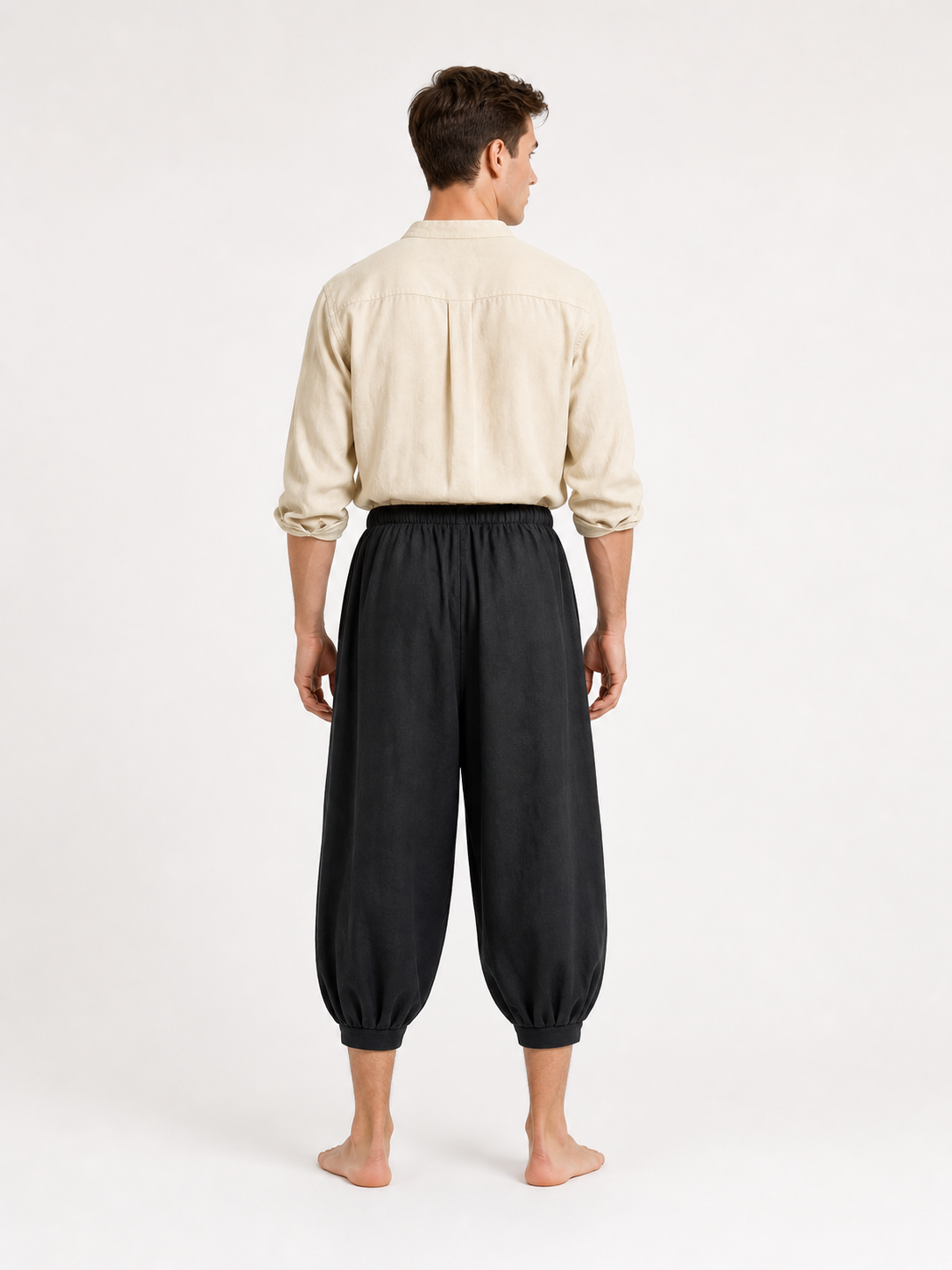 Back view of a man wearing black cropped harem pants with a gathered waistband, loose legs, and ankle cuffs