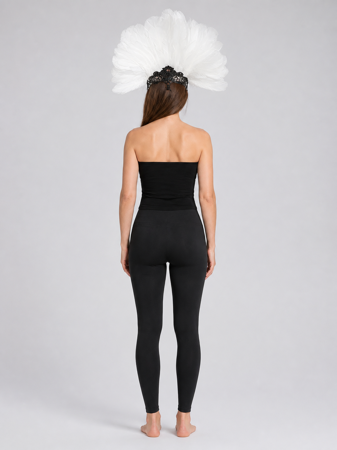 Back view of a model wearing the white feather headpiece with a black lace mask and a black fitted outfit