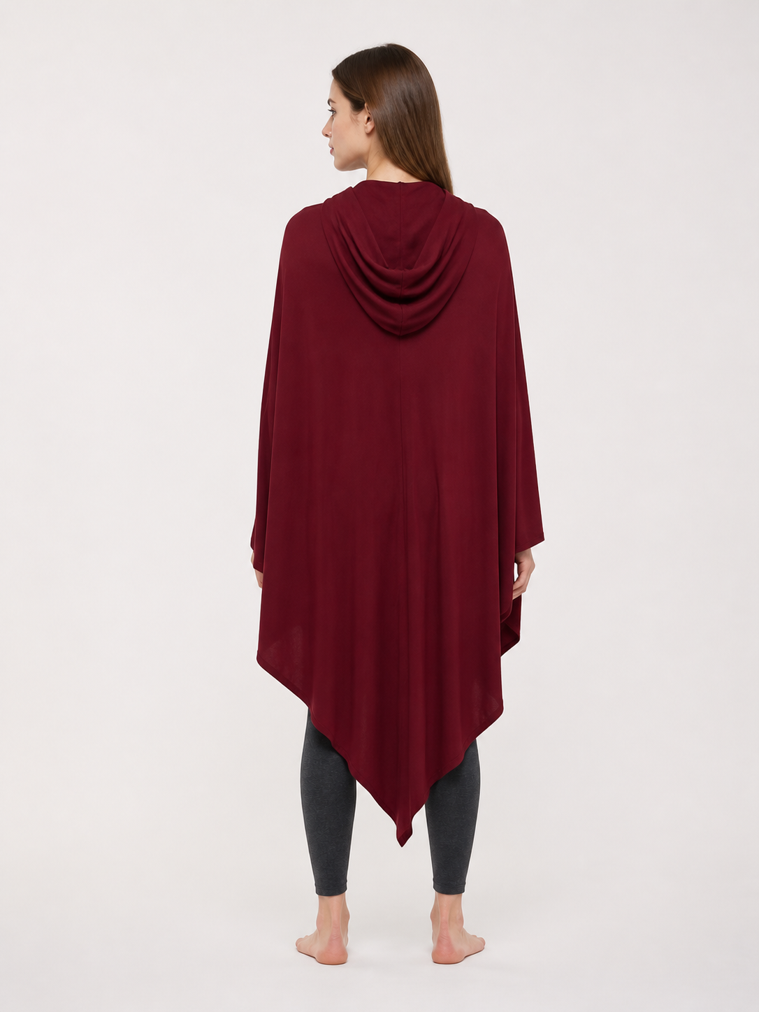 Back view of a burgundy hooded cloak with smooth drape and pointed hem, modeled in a gray studio