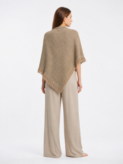 Back view of the beige woven cape worn with light shorts, showing the pointed drape and fringed edges