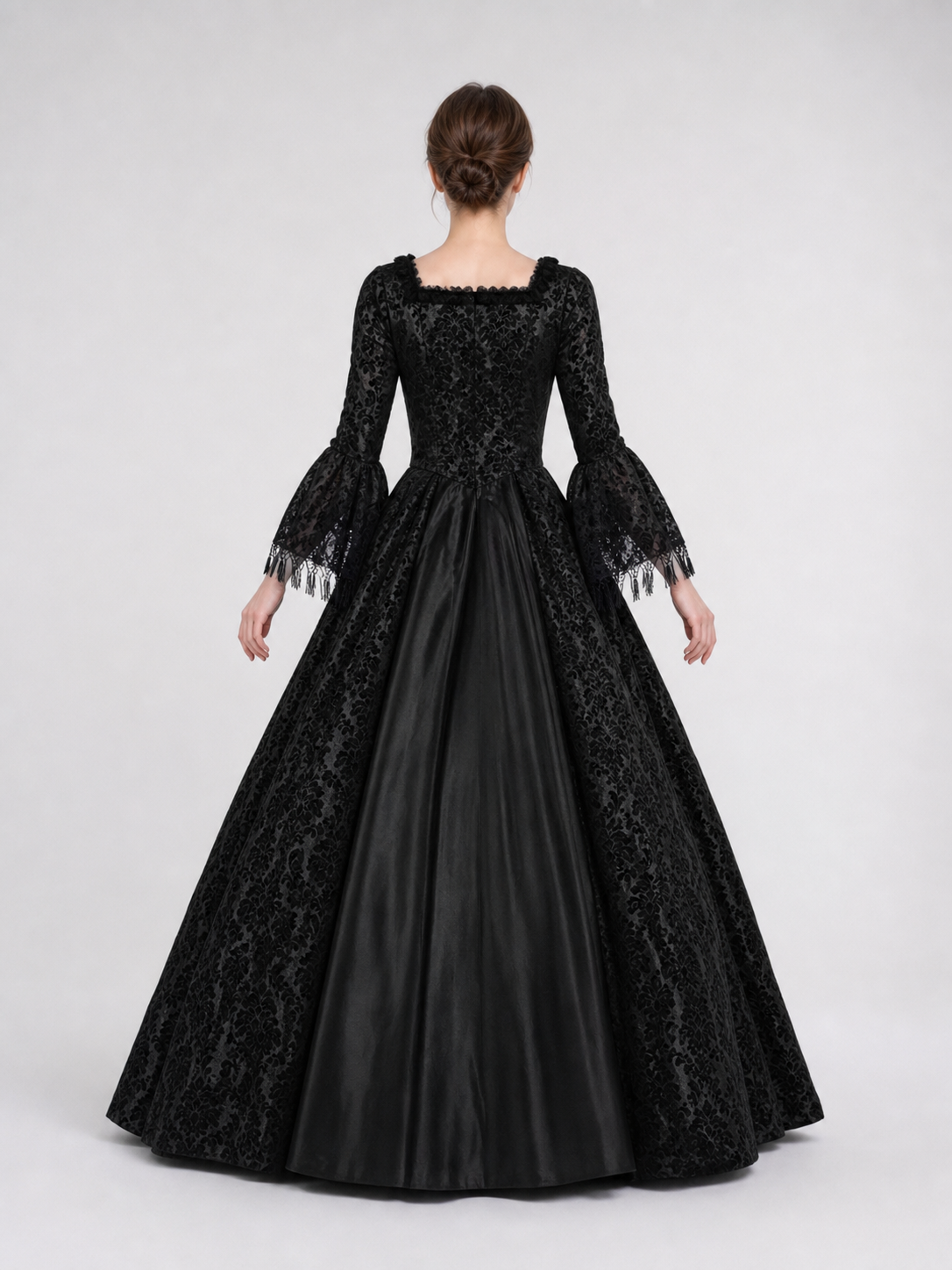 The black dress is designed in the aesthetic of a Victorian-era Gothic costume. The model features a floor-length silhouette, a fitted bodice with a square neckline, and decorative lacing or trim on the front. The long flared sleeves end in
