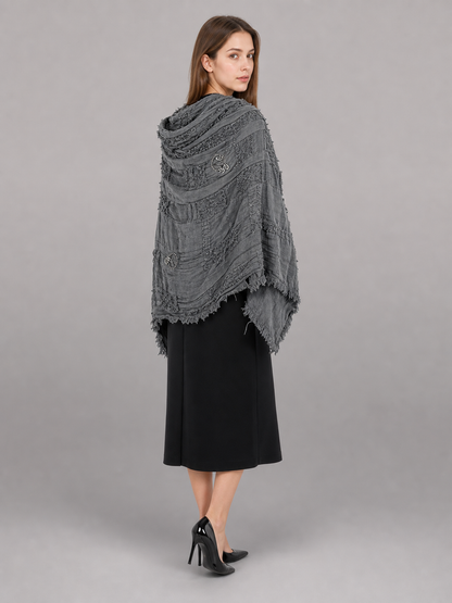 This large scarf-wrap is designed as a rectangular drape with a striking textured surface. The black-and-gray color palette is accented with lighter gray tones, giving the piece a distinctive look that pairs easily with different outfits. T