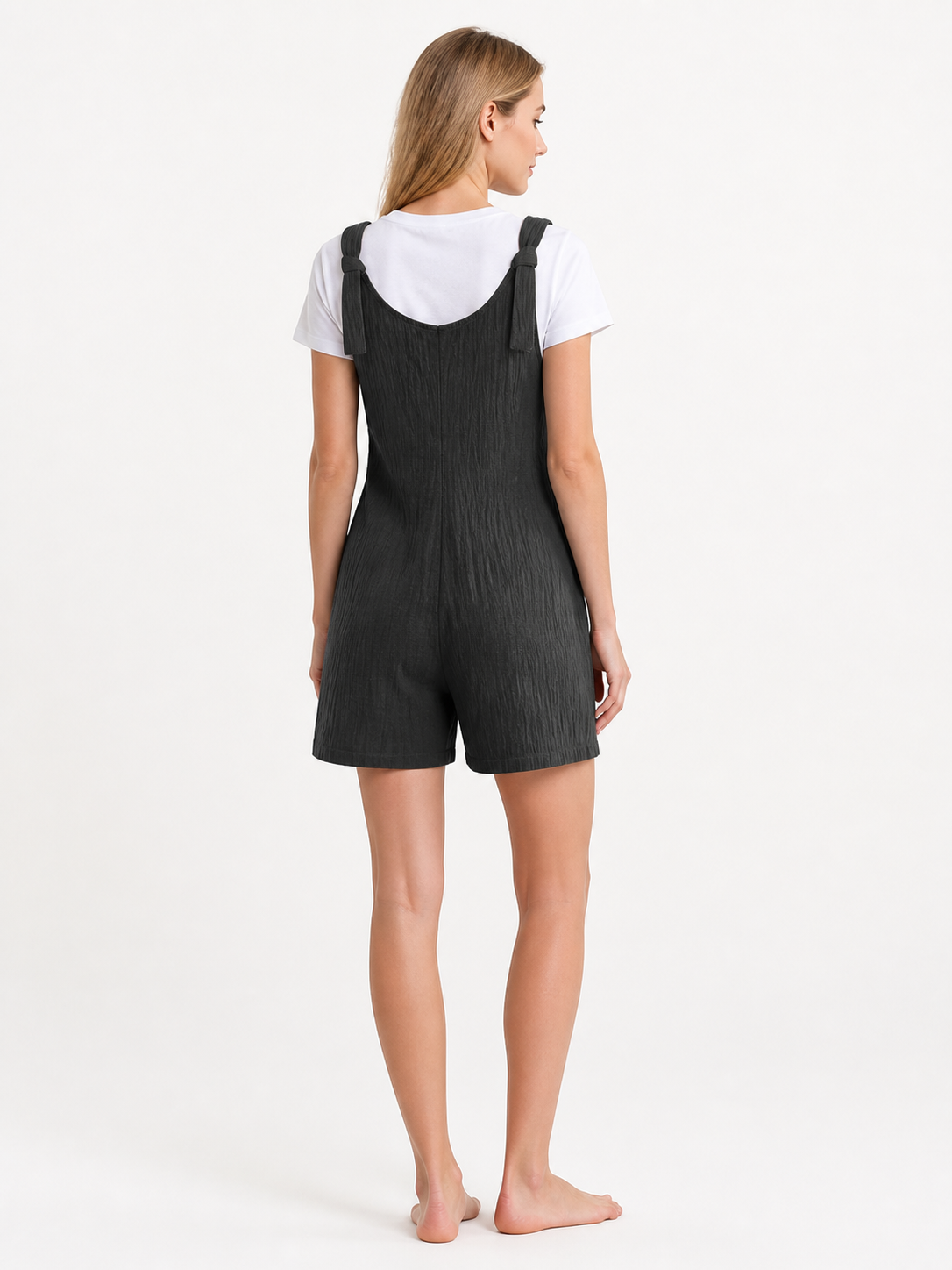Rear view of black bib shorts with wide shoulder straps and shorts-length legs, modeled over a white T-shirt