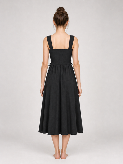 Back view of a black midi dress on a model with hair in a bun, showing wide straps, a square neckline, side ties, and a gathered skirt