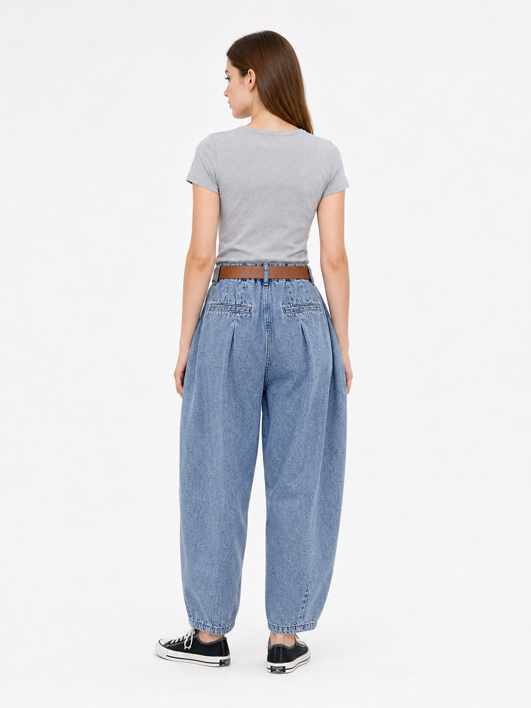 Back view of blue denim pants on a model, showing the high waistband, wide legs, rear seams, and black sneakers