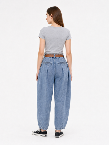 Back view of blue denim pants on a model, showing the high waistband, wide legs, rear seams, and black sneakers
