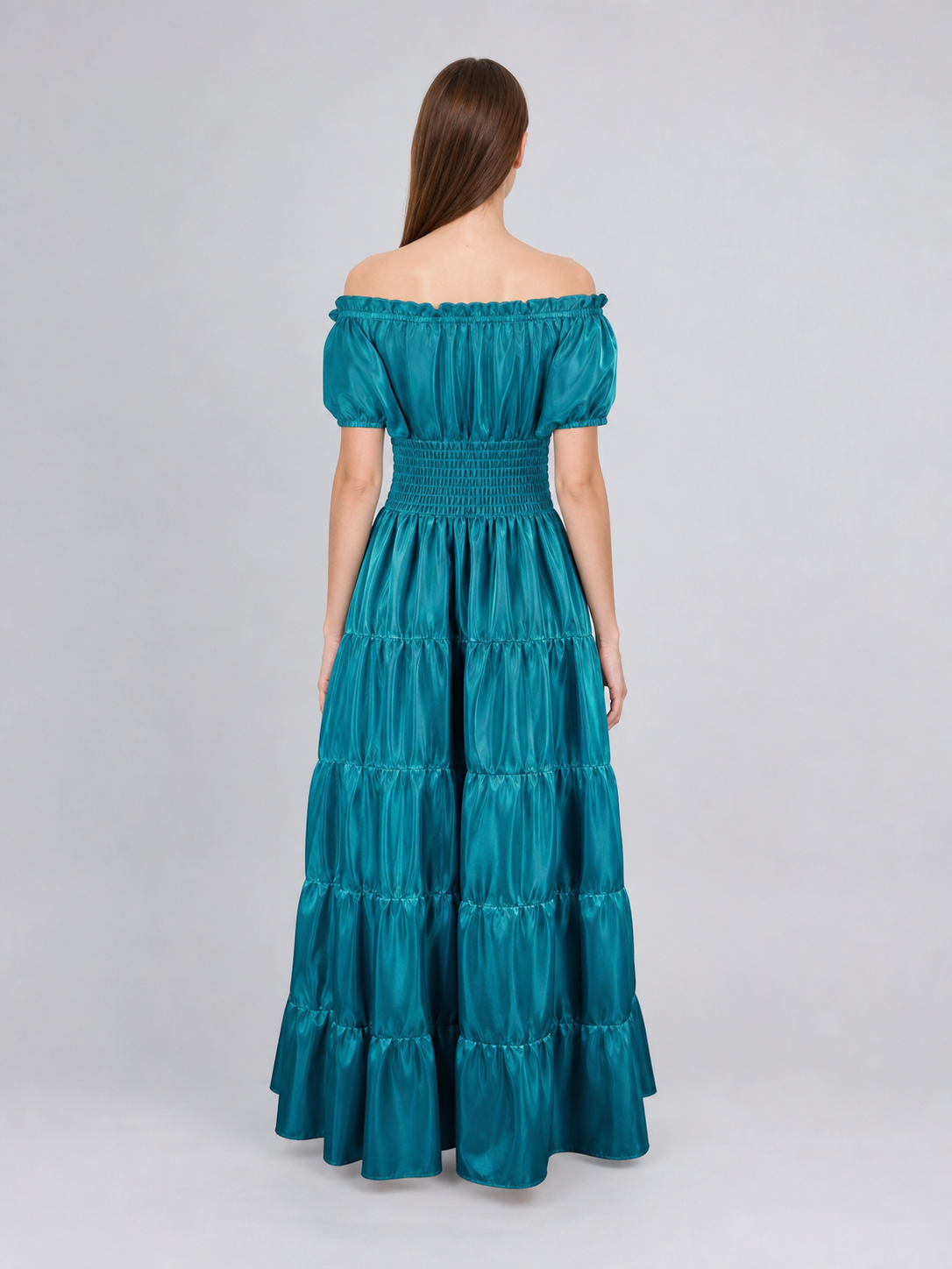 Rear view of a teal glossy maxi dress on a model, showing the elastic off-shoulder neckline, smocked waist, and long gathered skirt