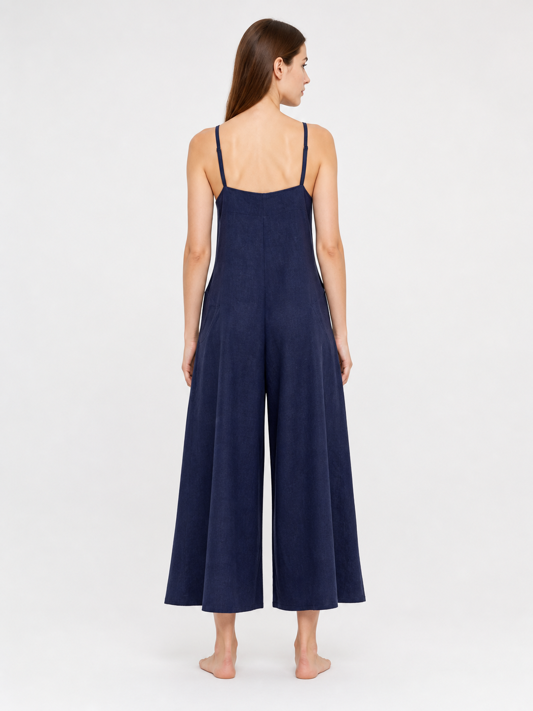 Rear view of a dark blue wide-leg jumpsuit on a model, showing thin straps, a straight back neckline, and flowing legs