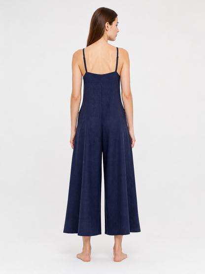 Rear view of a dark blue wide-leg jumpsuit on a model, showing thin straps, a straight back neckline, and flowing legs