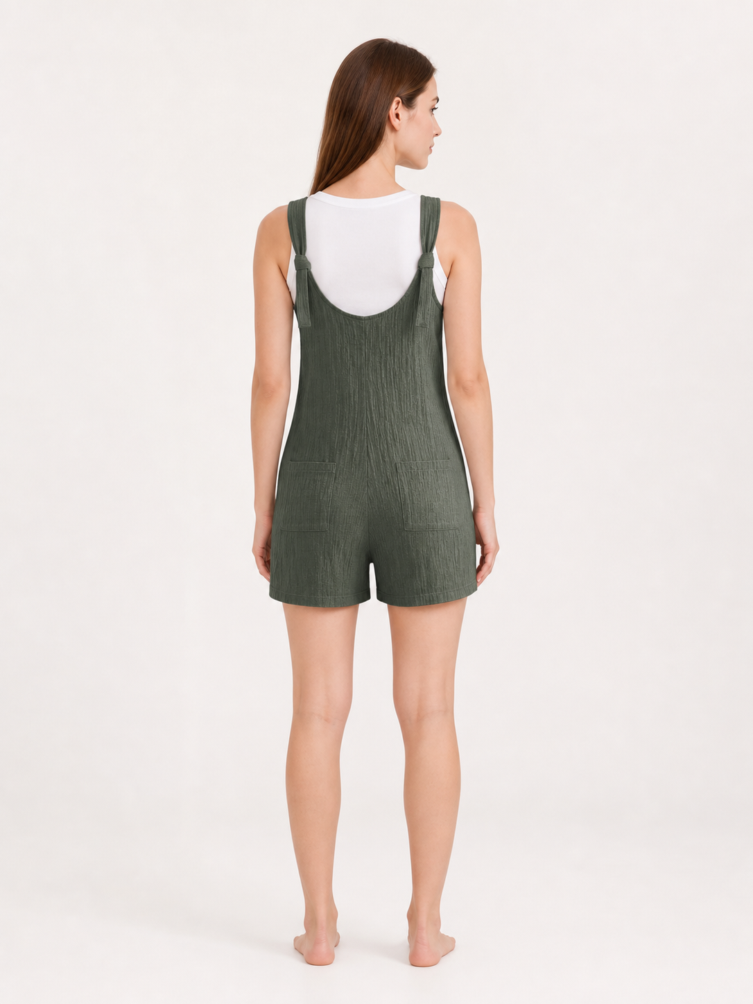 Back view of olive green textured overall shorts worn over a white T-shirt, showing the tied shoulder straps and loose short-leg silhouette