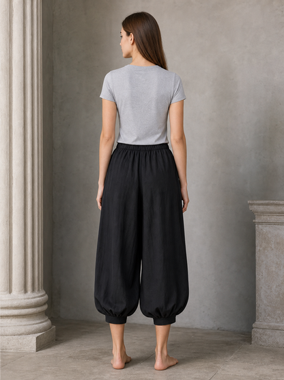 Back view of a woman wearing black cropped harem pants with a gathered waistband, loose legs, and elastic ankle cuffs