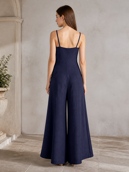 Rear three-quarter view of a dark blue wide-leg jumpsuit, showing thin straps, a low back, and wide flowing legs