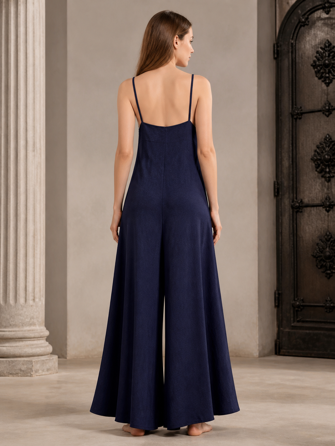 Rear view of a dark blue wide-leg jumpsuit on a model, showing the back neckline, thin straps, and wide legs