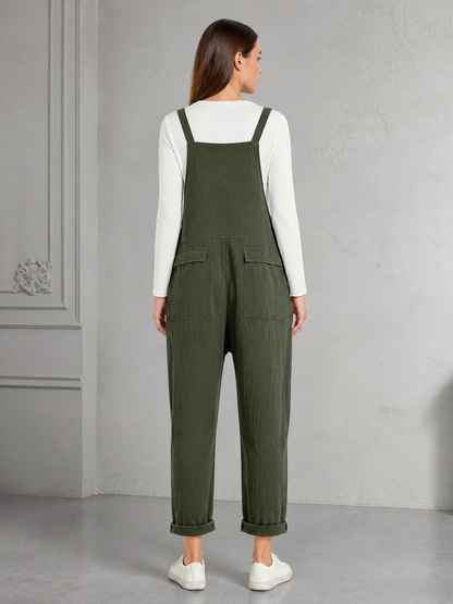 Back view of dark green bib overalls showing the wide back panel, shoulder straps, two rear pockets, rolled cuffs, and white sneakers