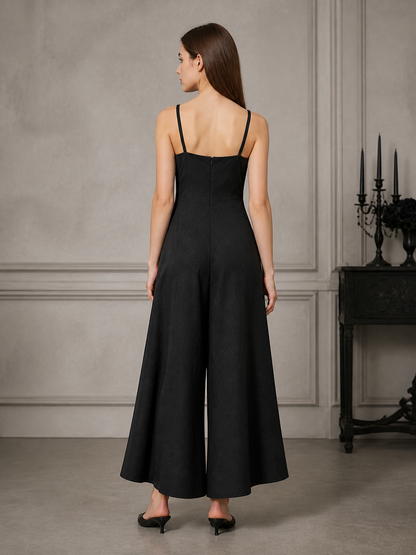 Back view of a black wide-leg jumpsuit with thin straps and a center seam, modeled in a gray paneled room