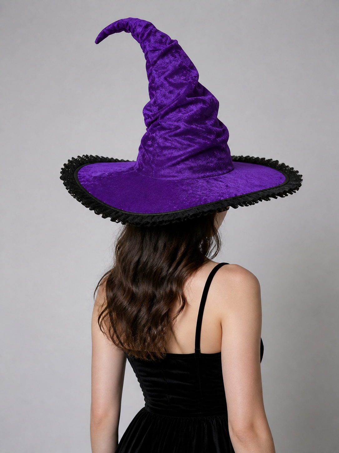Rear angled view of a purple pointed witch hat with a wide brim and black trim, worn by a model in a black top