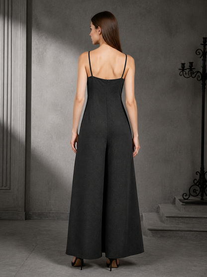 Back view of a black wide-leg jumpsuit showing thin straps, a fitted upper section, and flowing wide legs against a dark interior