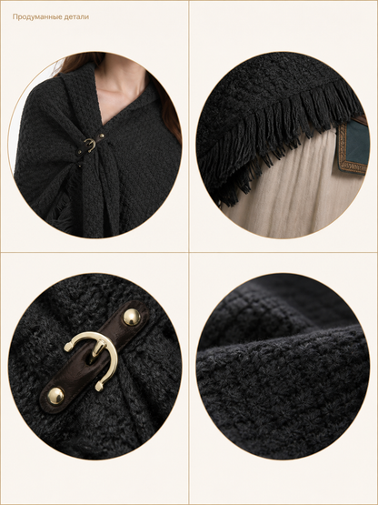Black knitted poncho cape styled on a model with black pants and tall boots in an indoor scene, showing fringe and a pointed front