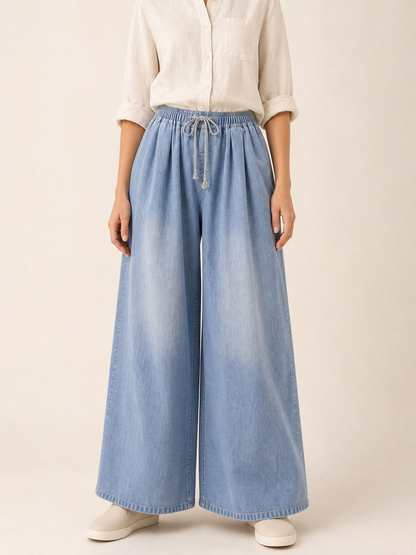 The model features a relaxed style with very wide, full-length legs that create a laid-back silhouette and suit everyday looks. The light blue shade with a subtle denim-like effect makes the piece versatile for warm weather and easy to pair