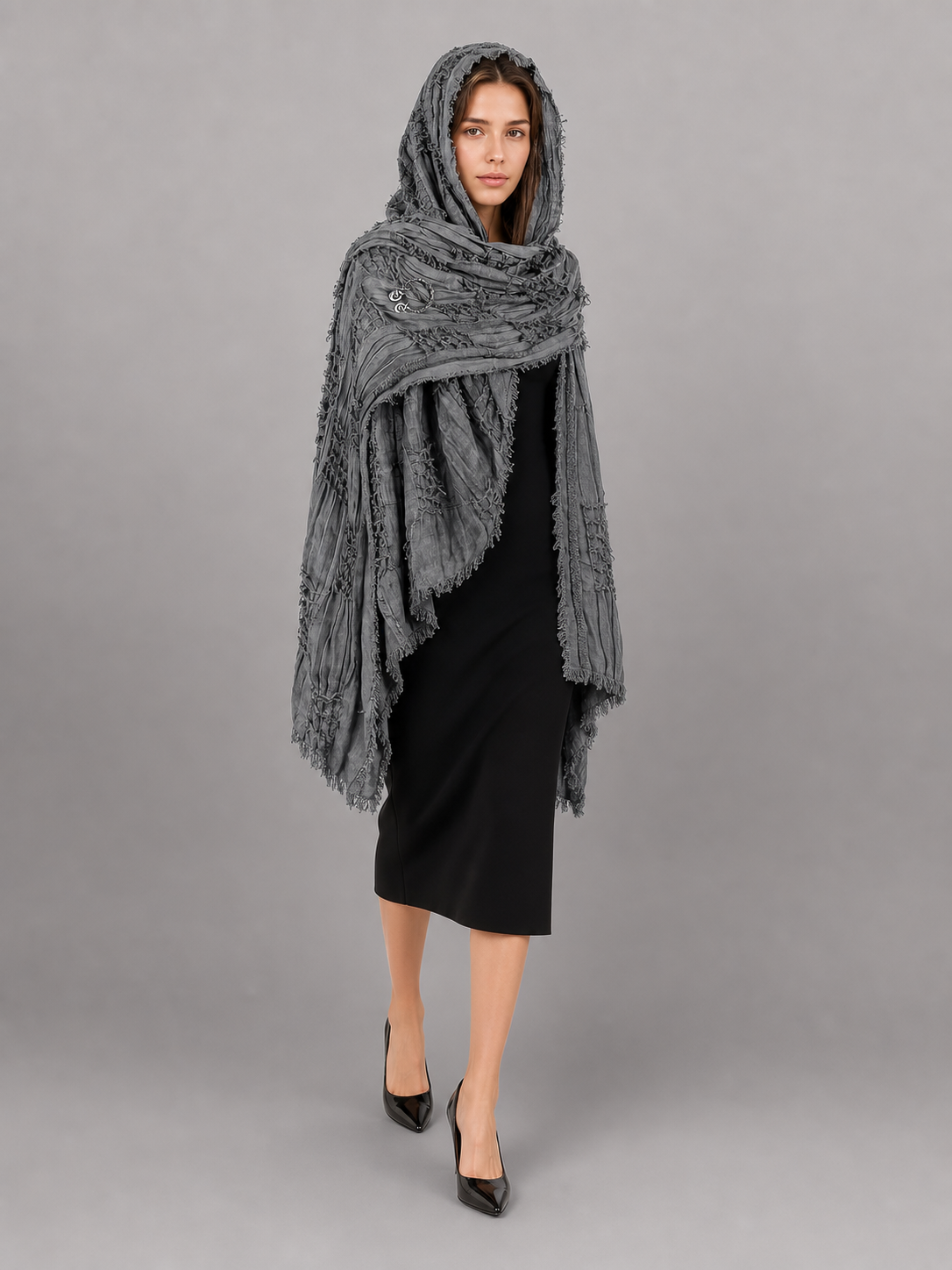 This large scarf-wrap is designed as a rectangular drape with a striking textured surface. The black-and-gray color palette is accented with lighter gray tones, giving the piece a distinctive look that pairs easily with different outfits. T