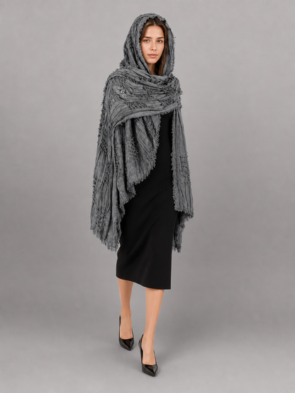 This large scarf-wrap is designed as a rectangular drape with a striking textured surface. The black-and-gray color palette is accented with lighter gray tones, giving the piece a distinctive look that pairs easily with different outfits. T