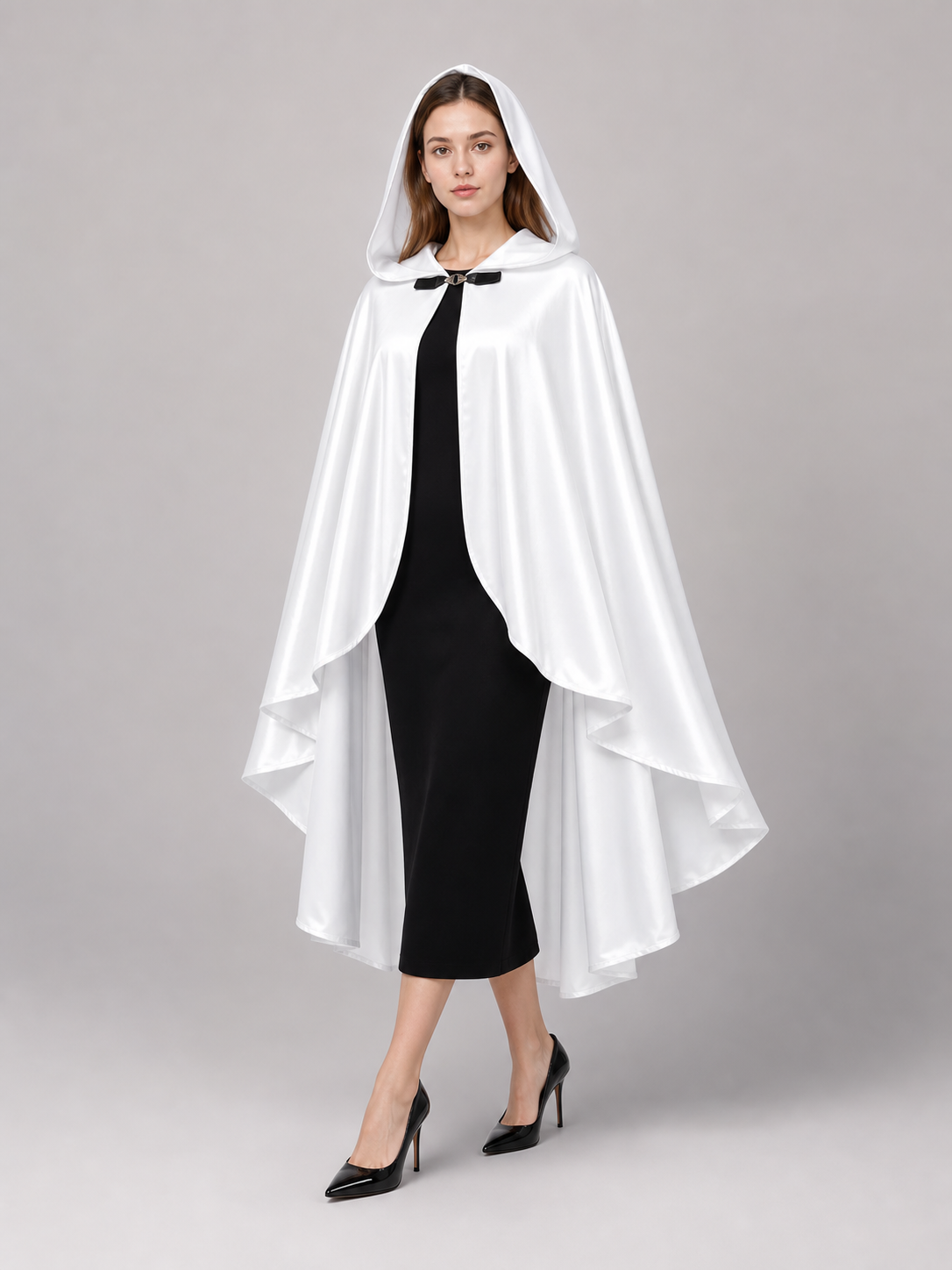 White hooded cape with flowing layered hem and black toggle closure, modeled in profile over a black dress with pointed heels
