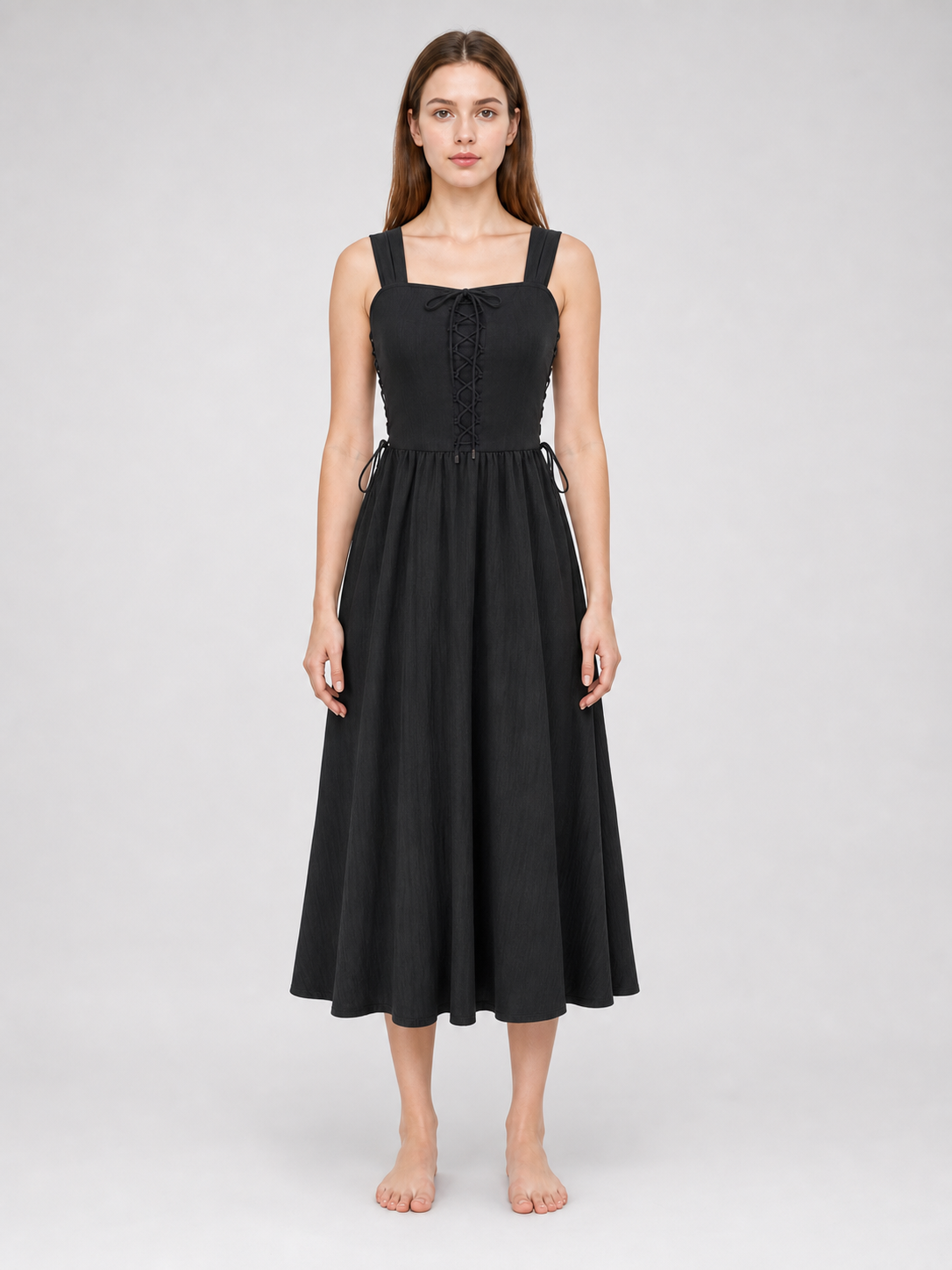 Front view of a black midi dress on a model, featuring a square neckline, lace-up bodice, side waist ties, and a wide flowing skirt