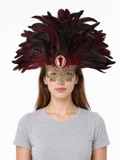 Front-facing model wearing a burgundy and black feathered mask headpiece with ornate gold filigree and a red oval jewel