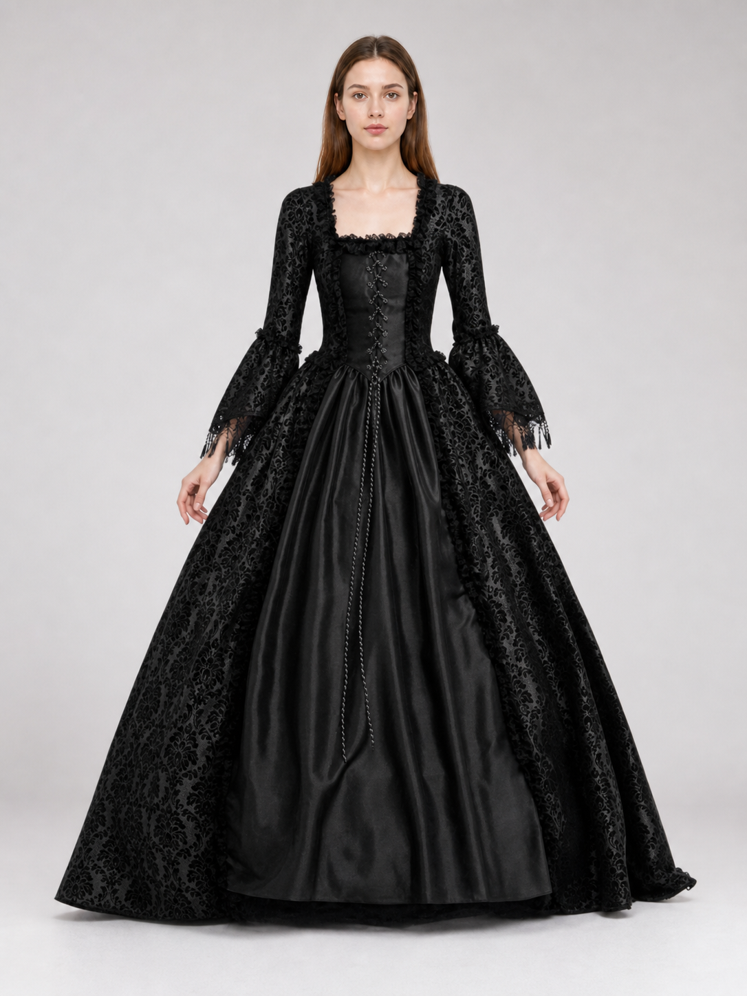 The black dress is designed in the aesthetic of a Victorian-era Gothic costume. The model features a floor-length silhouette, a fitted bodice with a square neckline, and decorative lacing or trim on the front. The long flared sleeves end in