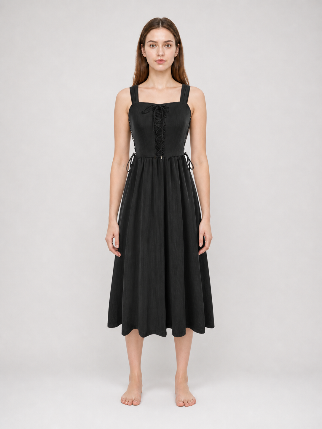 Black midi dress shown full-body on a model, with a fitted lace-up bodice, broad straps, adjustable side ties, and a flared hem