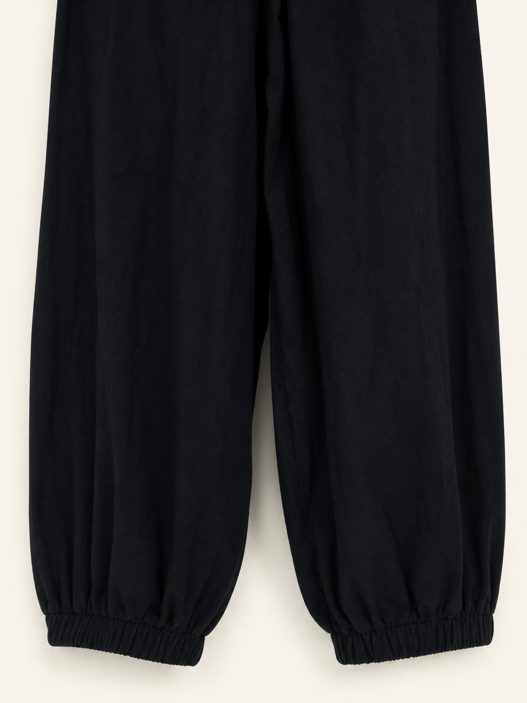 Close-up of the lower legs of black cropped pants laid flat, showing gathered elastic ankle cuffs