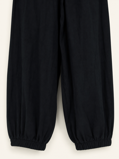 Close-up of the lower legs of black cropped pants laid flat, showing gathered elastic ankle cuffs