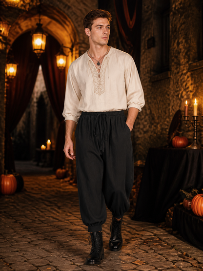 Man wearing black cropped harem pants with a drawstring waistband and side pockets, styled with a cream shirt and boots in a stone interior