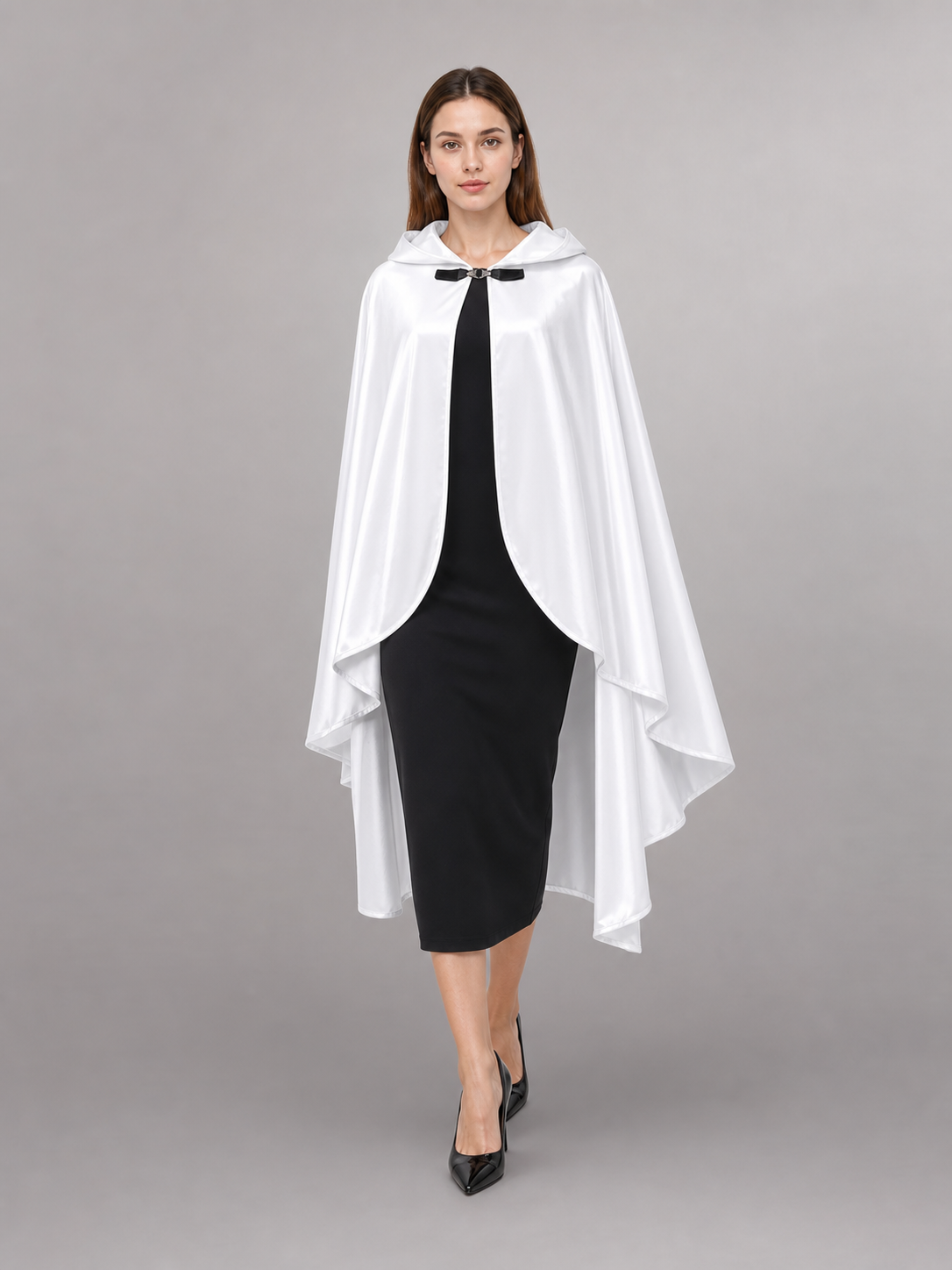 White hooded cape with flowing layered sides and black toggle closure, shown on a walking model wearing a fitted black dress and heels