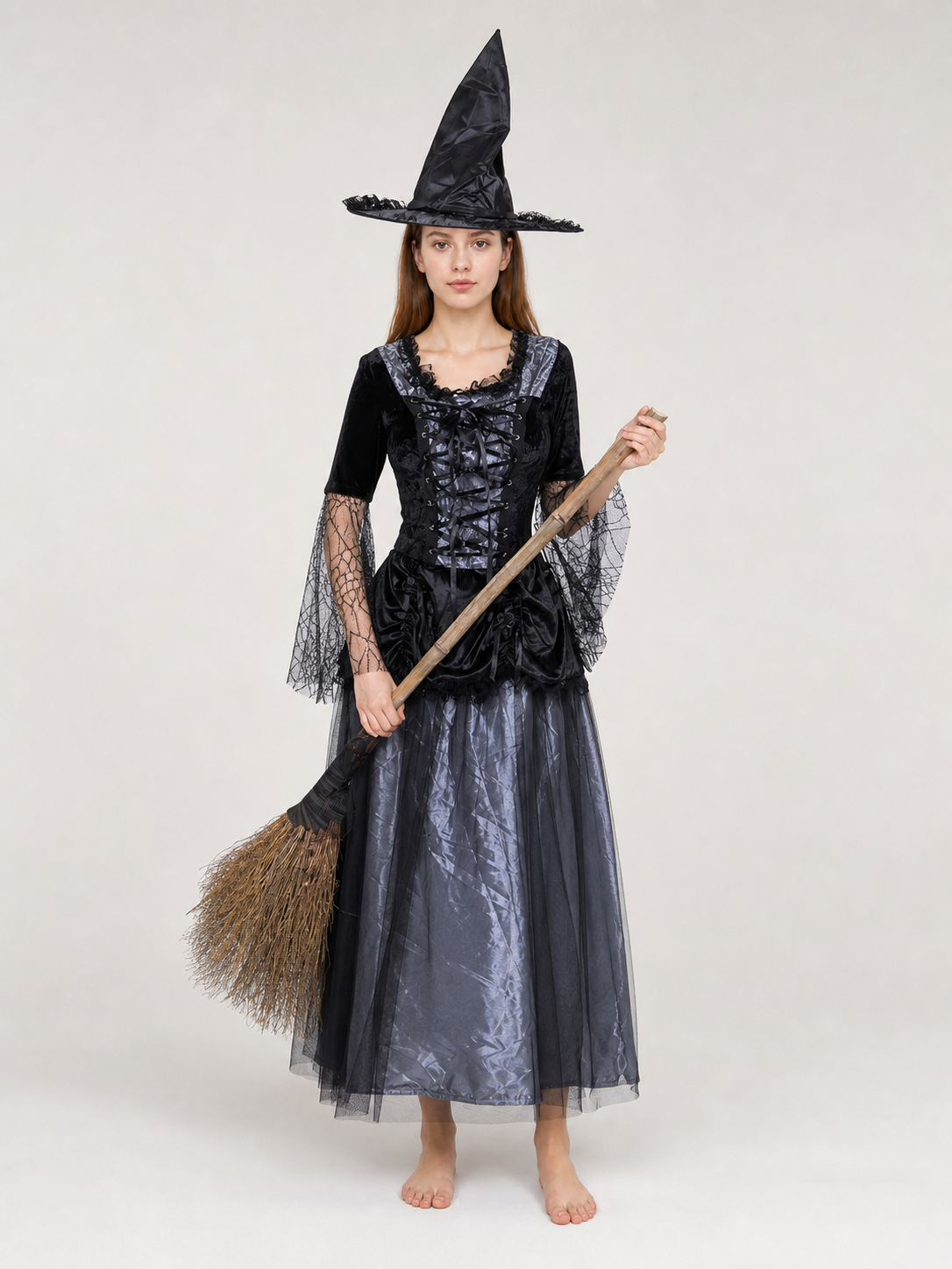 Gothic-style witch costume dress with hat for themed events. The design is mainly black and dark gray, with patterned textured fabric and sheer black accents. The look is centered on a long dress with a fitted lace-up corset, a ruffled neck