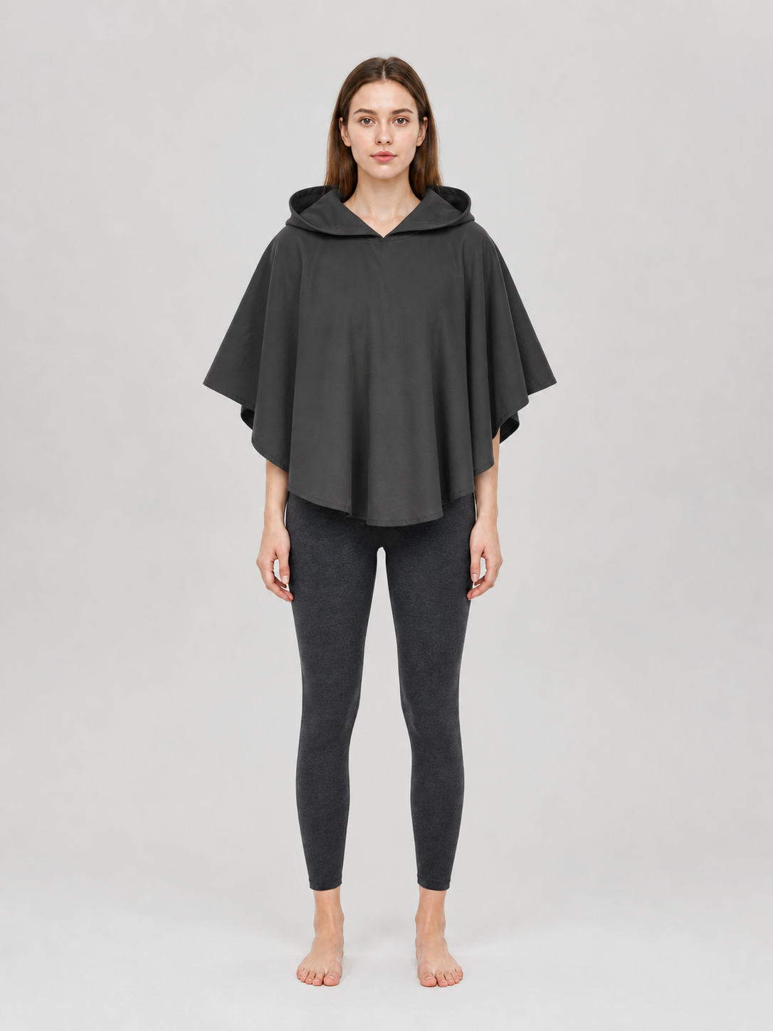 Dark gray hooded poncho with a loose draped fit, shown full-body on a female model in a studio